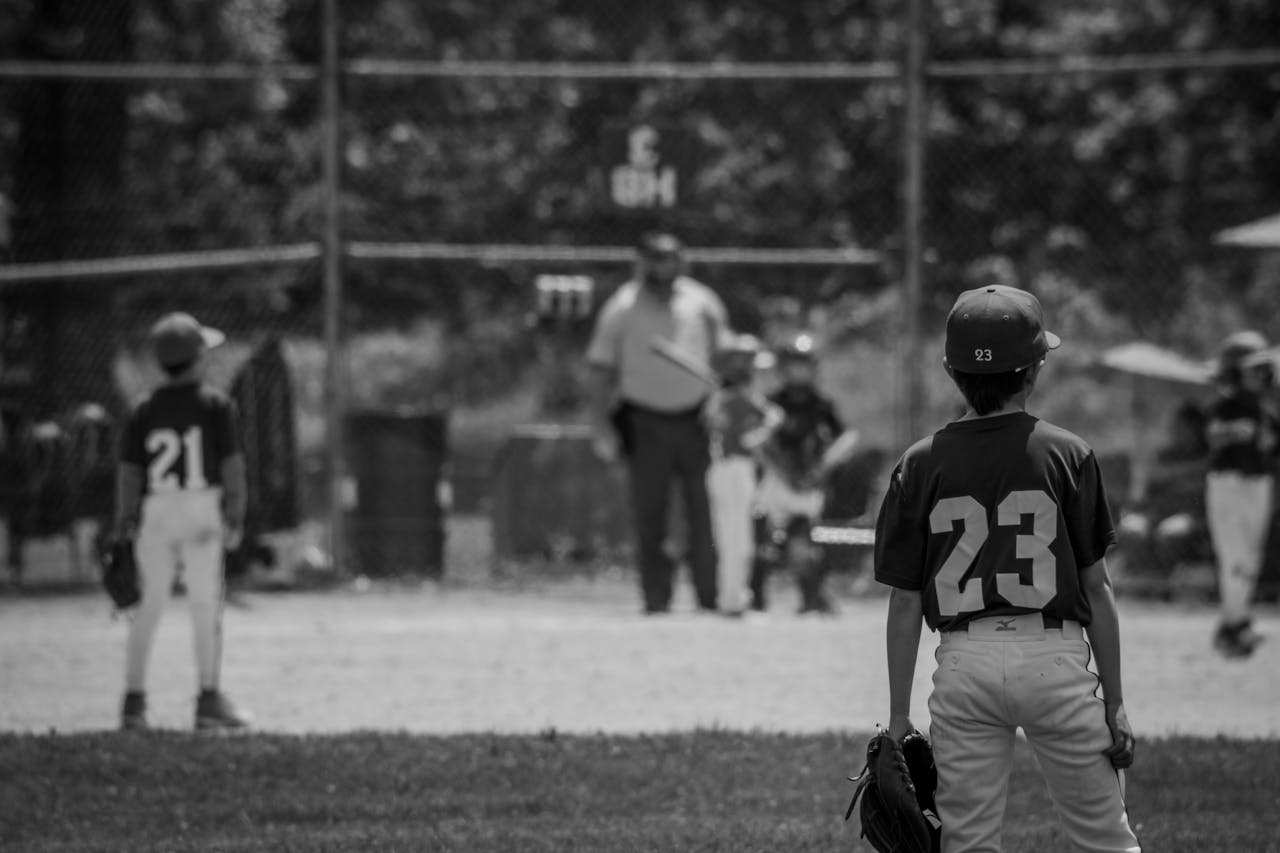 hero-img-02 Monochrome scene of young baseball players on a field with uniforms and equipment.