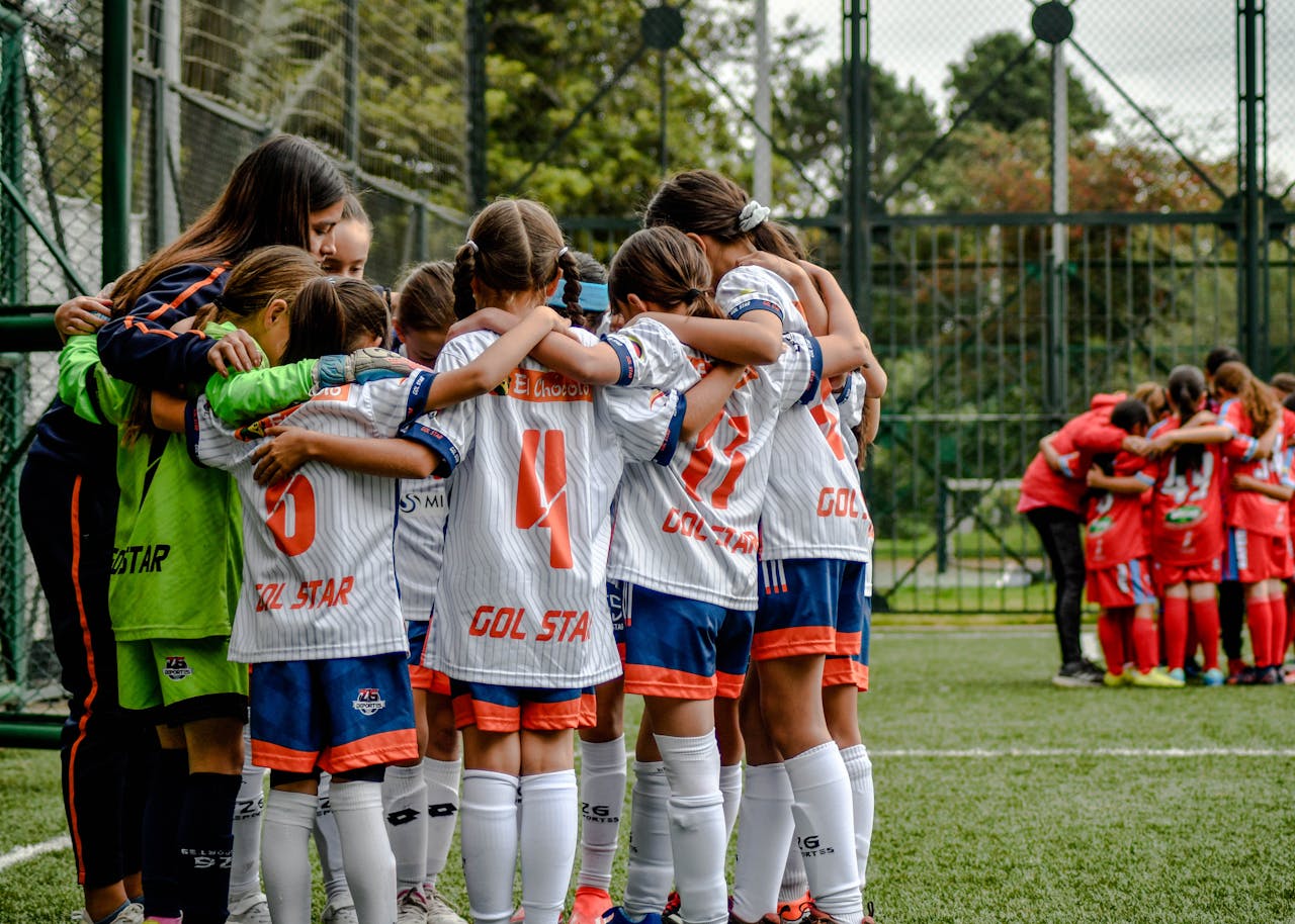 gallery-1 Young soccer team in white uniforms huddling on field, fostering teamwork.
